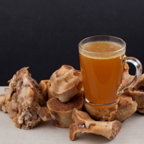 Transparent Cup of bone broth is placed on boiled beef bones
